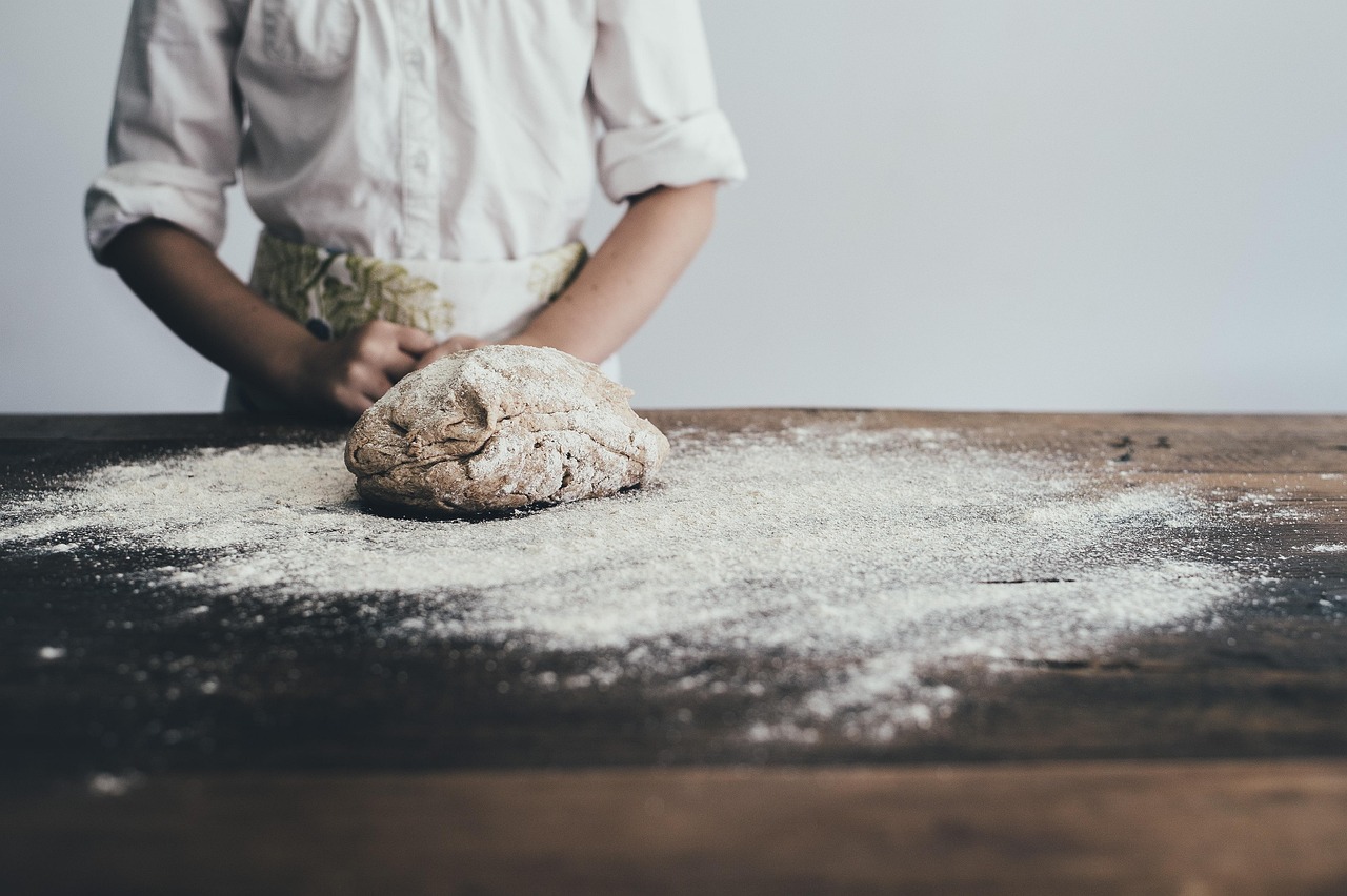 Baker in an apron kneading dough on a floured wooden table